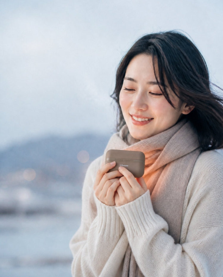 寒い朝、リベティの充電式カイロを両手で包んでほっと温まる女性